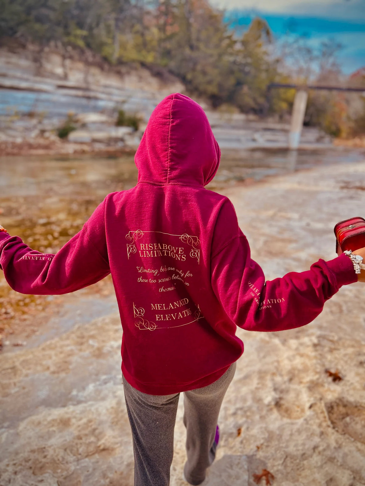 Model outdoors wearing the burgundy Melanated Elevation hoodie with the back design visible